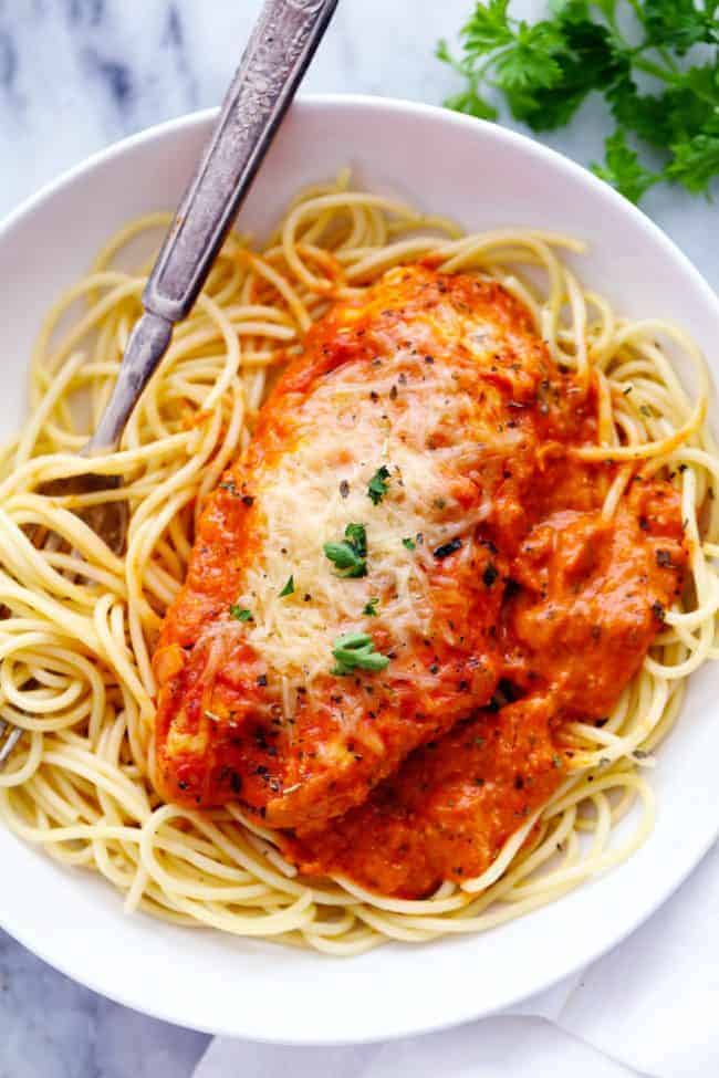 Creamy Tomato Italian Parmesan Chicken over noodles in a white bowl and a metal fork. 