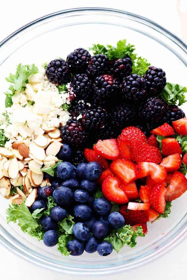 Triple Berry Kale Salad ingredients in a large clear bowl. 