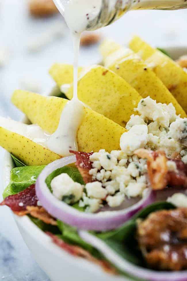 Grilled Chicken, Bacon, and Pear Salad with Poppyseed dressing being poured on top. 