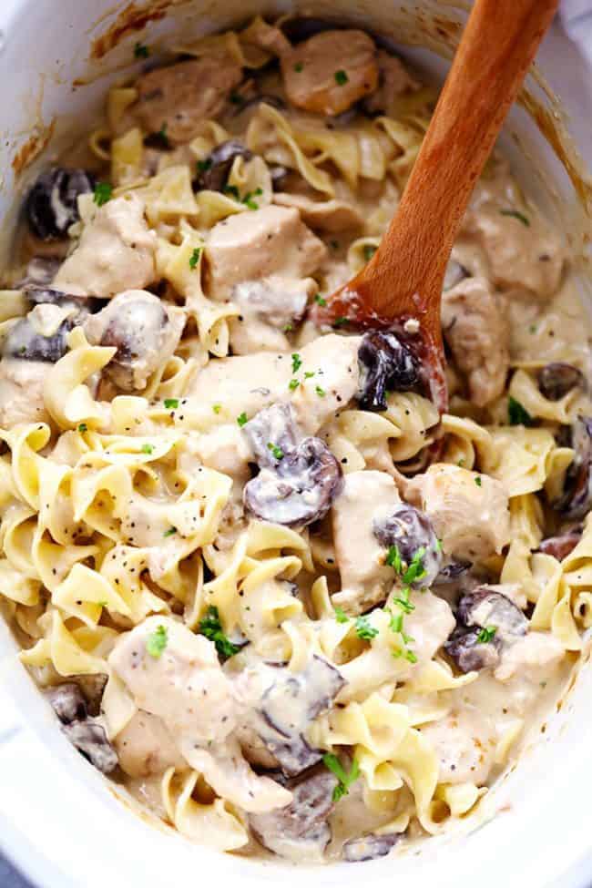 Chicken and mushroom stroganoff in a slow cooker being stirred by a wooden spoon. 