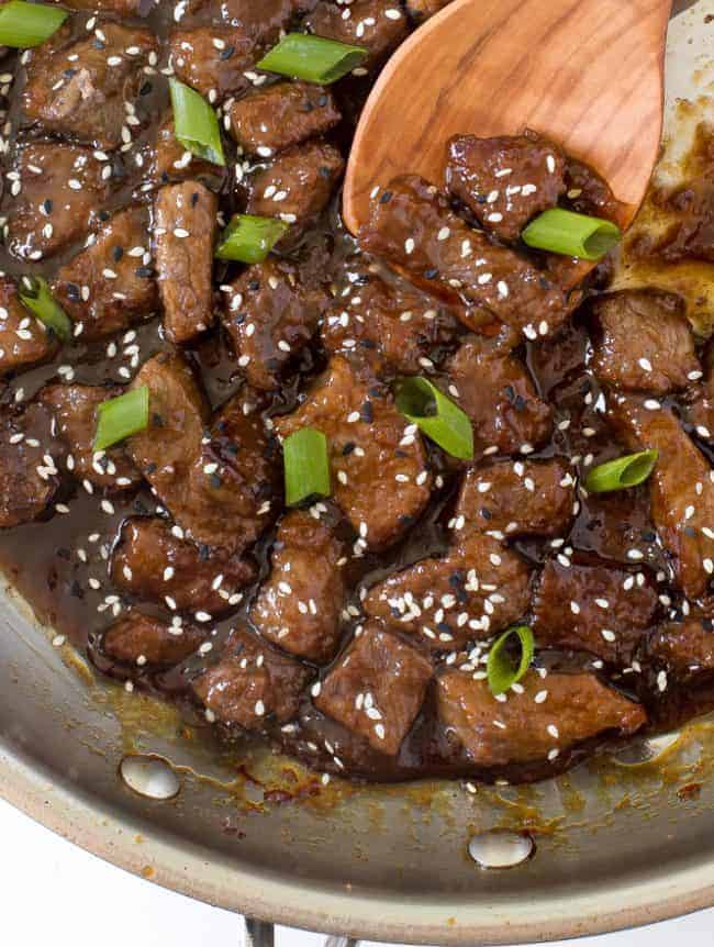 Teriyaki beef in a skillet with a wooden spoon.