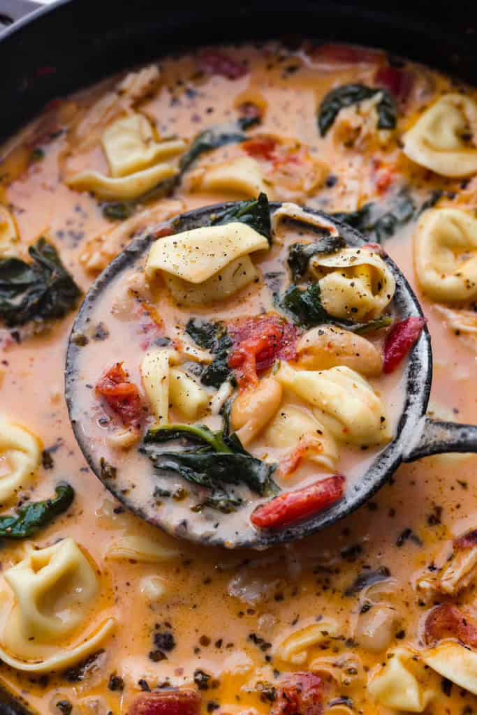 Close up shot of a ladle scooping a scoop of creamy Tuscan garlic tortellini soup above the pot. 