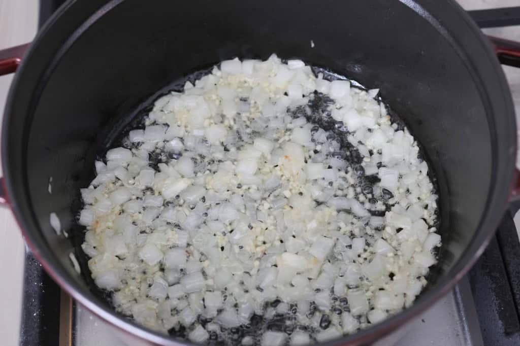 Overhead shot of melted butter, onions, and garlic in a pot being sautéed. 