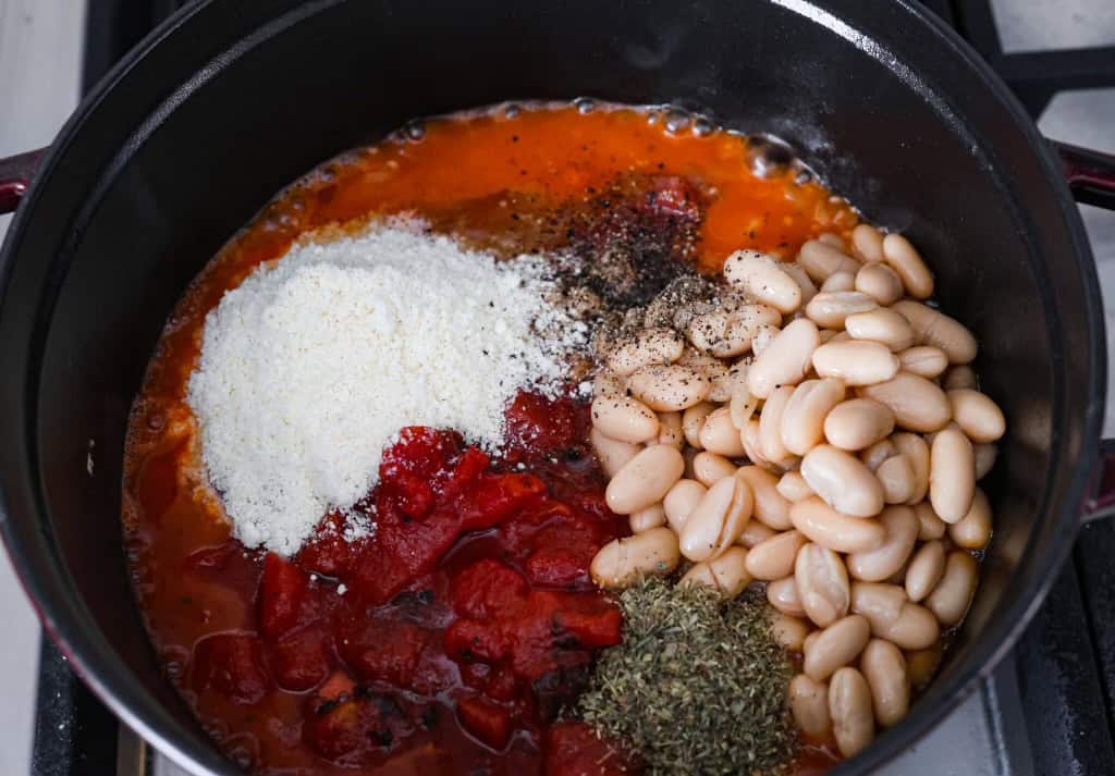 Overhead shot of beans, dice tomatoes, cheese seasonings and chicken broth added to the pot with onions and garlic. 