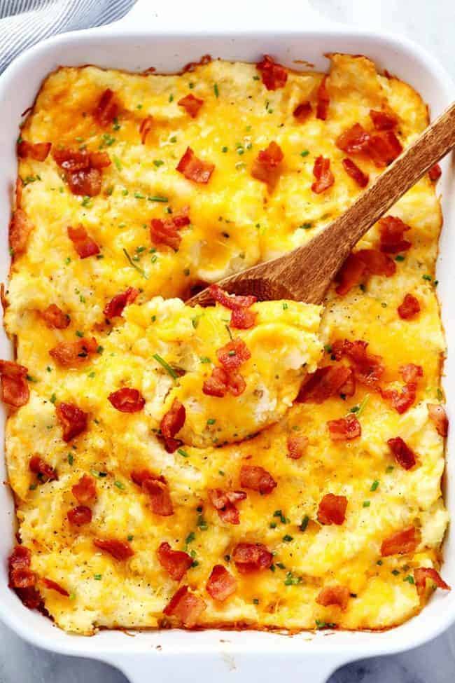 Cheddar Garlic Mashed Potato Casserole in a white casserole dish with a wooden spoon in the breakfast.