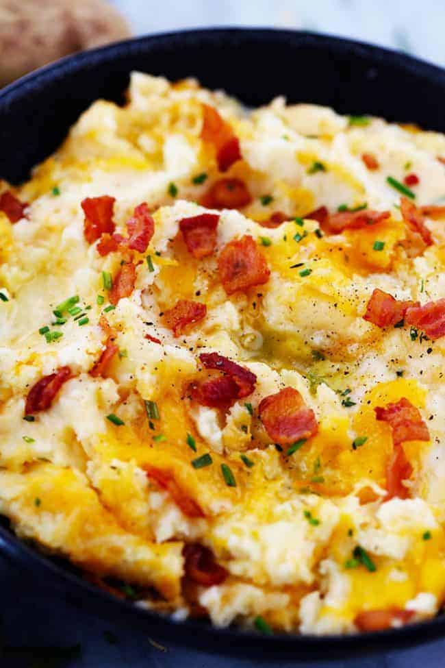 Mashed potatoes with bacon pieces as a garnish in a black bowl. 