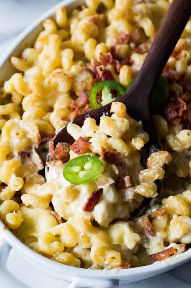 Jalapeño popper macaroni and cheese and a white casserole dish with a wooden spoon.