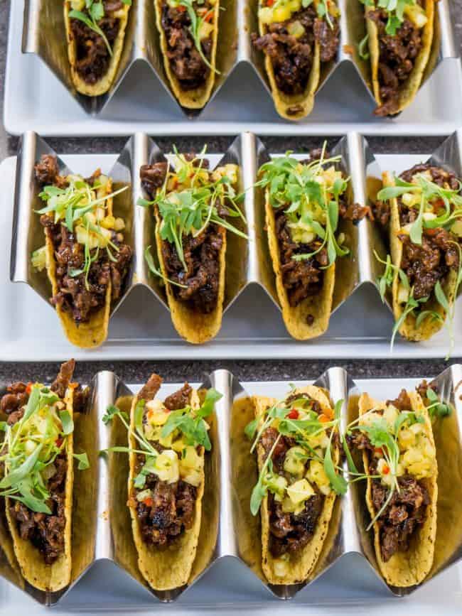 Rows of hardshell tacos with meat and lettuce on dividers.