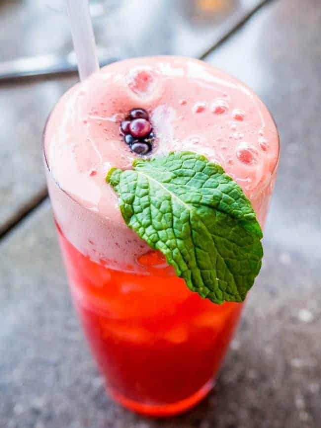 Lemonade with a straw and a mint leaf hanging out on the side of the cup. 