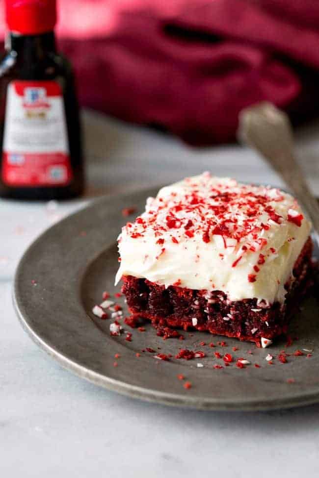 A slice of red velvet peppermint brownies with peppermint cream cheese frosting and a gray plate.