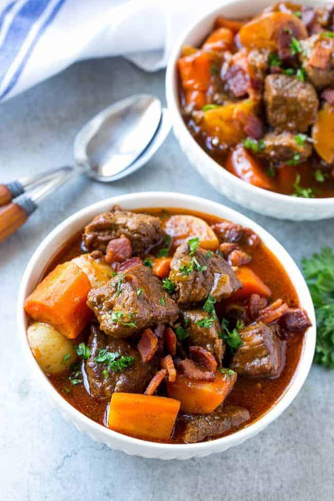 Beef stew with bacon and a white bowl.