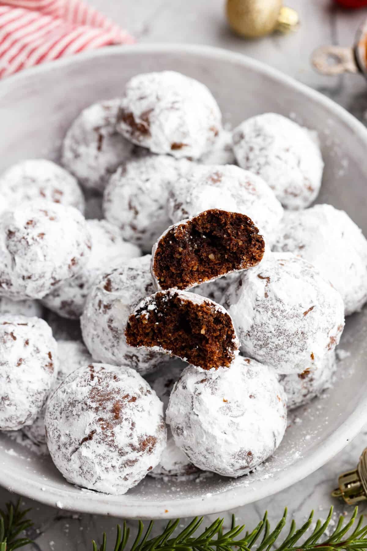 Close view of chocolate snowball cookies in a serving bowl with a cookie broken in half.