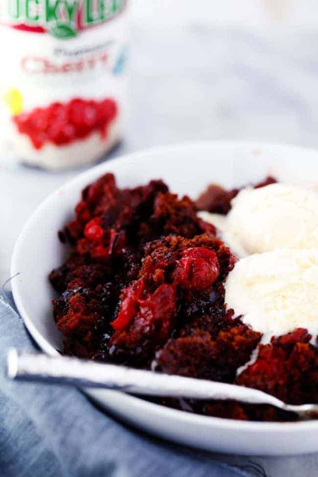 Slow cooker cherry chocolate half page cake in a white bowl with two scoops of ice cream on top and a spoon on the side.