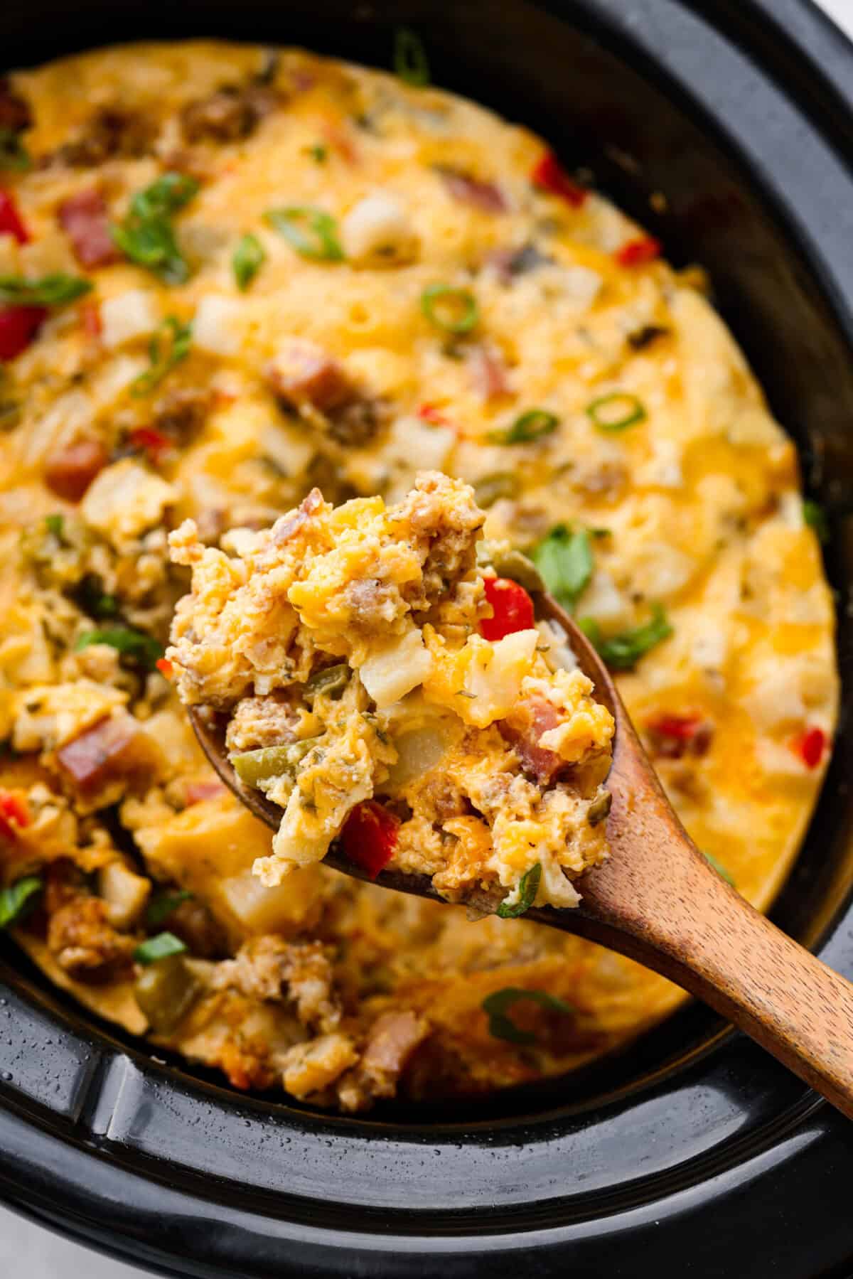 Close up shot of a scoop of slow cooker breakfast casserole on a wooden serving spoon. 