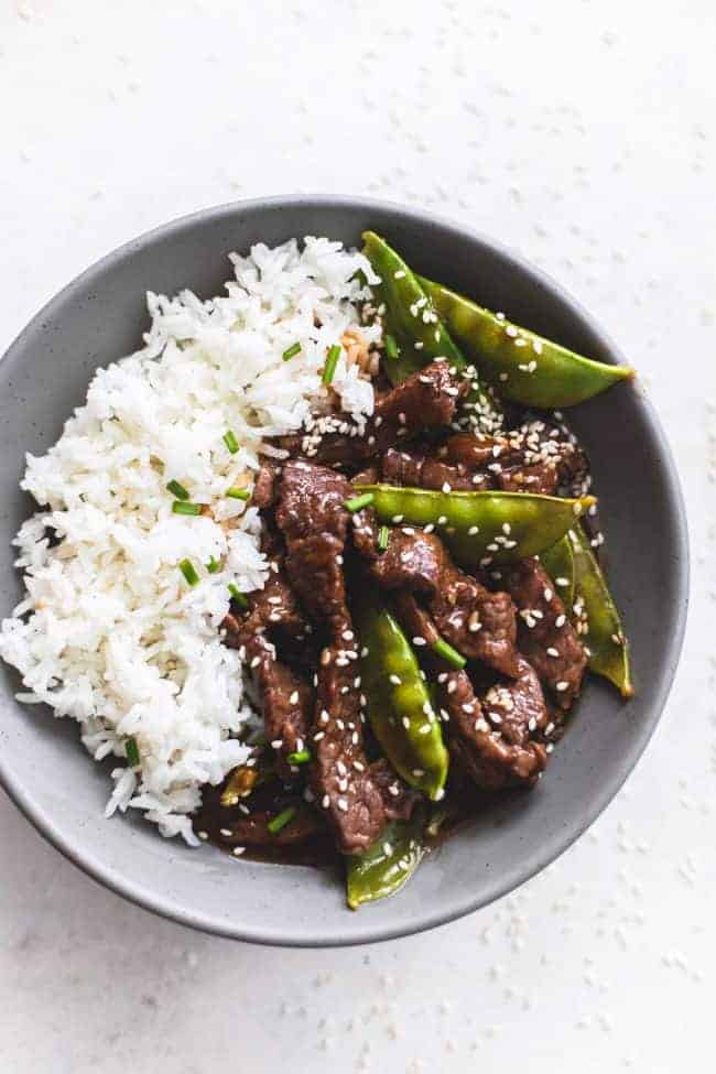 Honey sesame beef on a black plate with white rice.