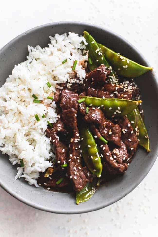 Honey sesame beef with rice on a black plate.