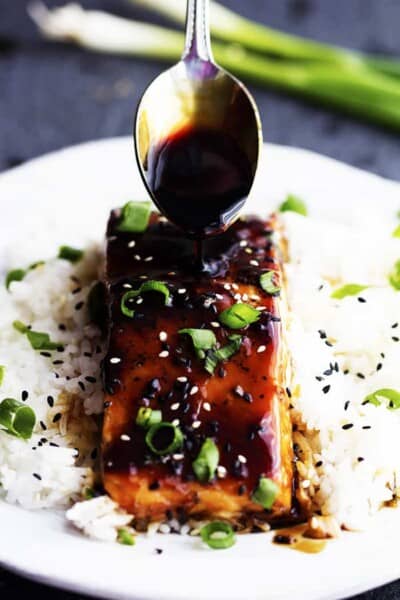 Baked Sesame Teriyaki Salmon on rice with a spoon pouring glaze on the salmon.