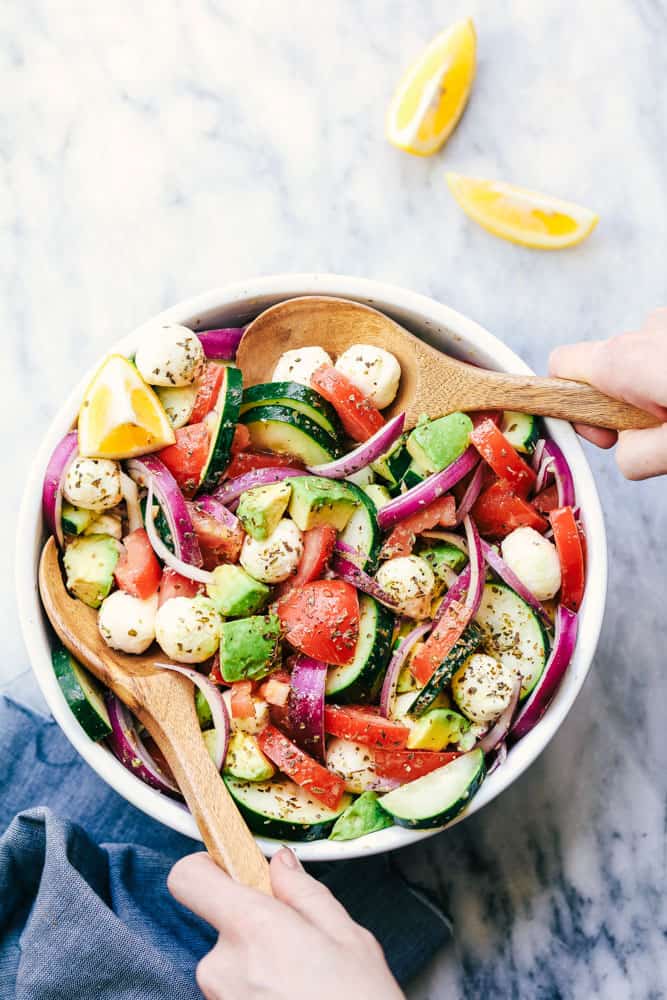 Italian Avocado Cucumber Tomato Salad in a white bowl with 2 wooden serving spoons.