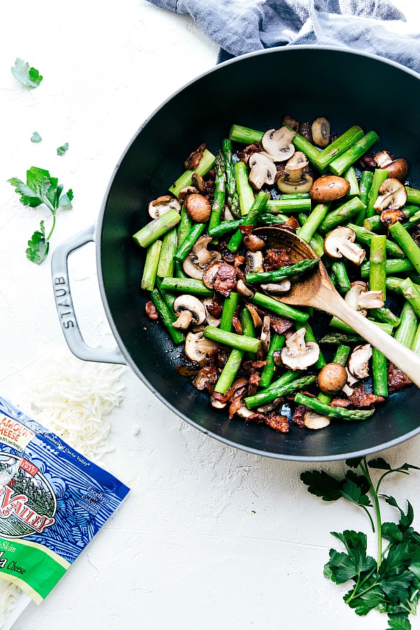 Cheesy Chicken, Asparagus, Bacon, and Mushroom Shells in a skillet being stirred with a wooden spoon.