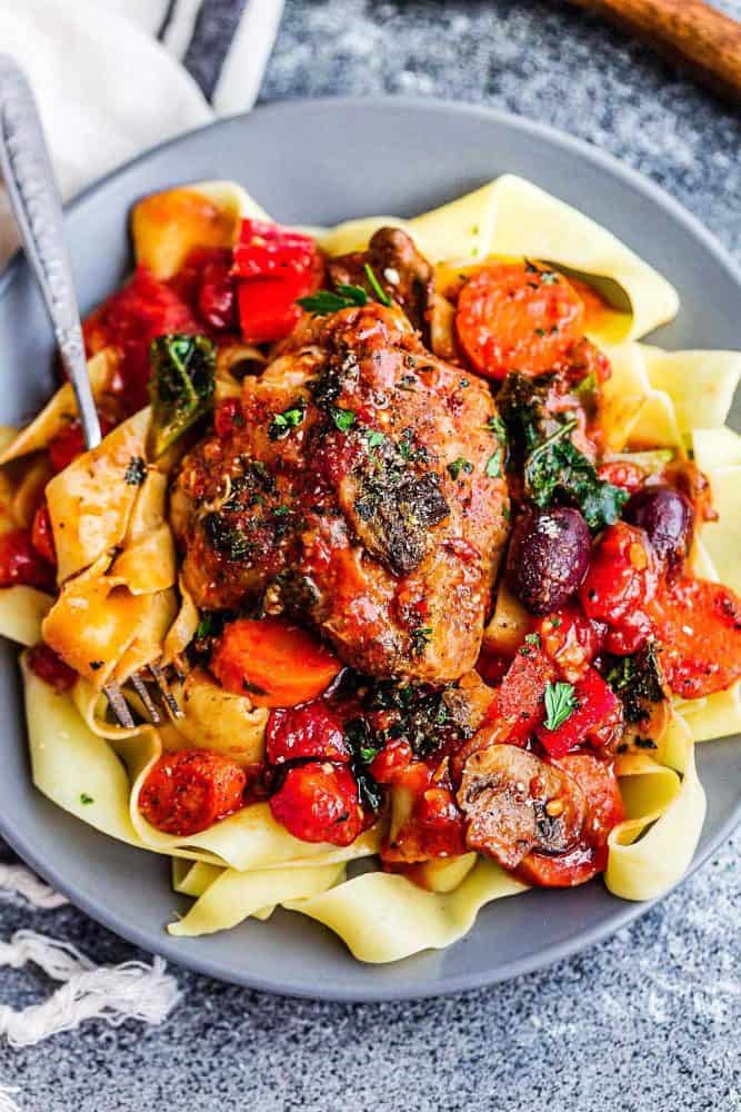 Slow Cooker Chicken Cacciatore over noodles on a gray plate.