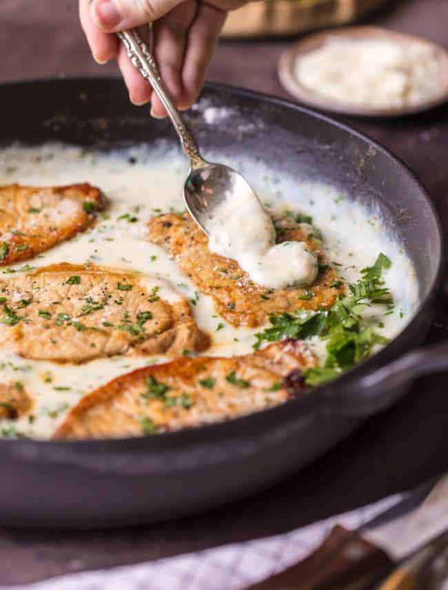 These Creamy Parmesan Pork Chops with a spoon pouring sauce over the pork chops in a skillet.