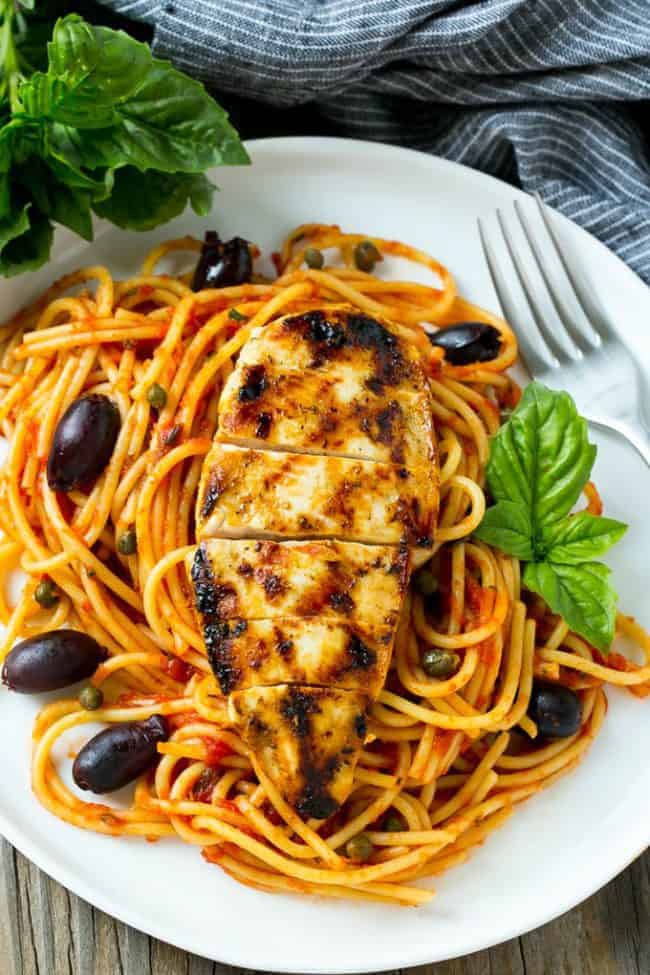 A white plate with pasta puttanesca. 