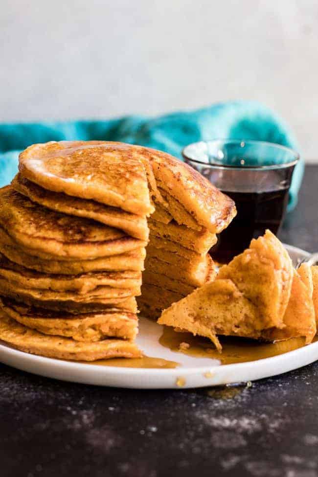 Maple Sweet Potato Pancakes stacked on a white plate with a bite cut out of the stack.