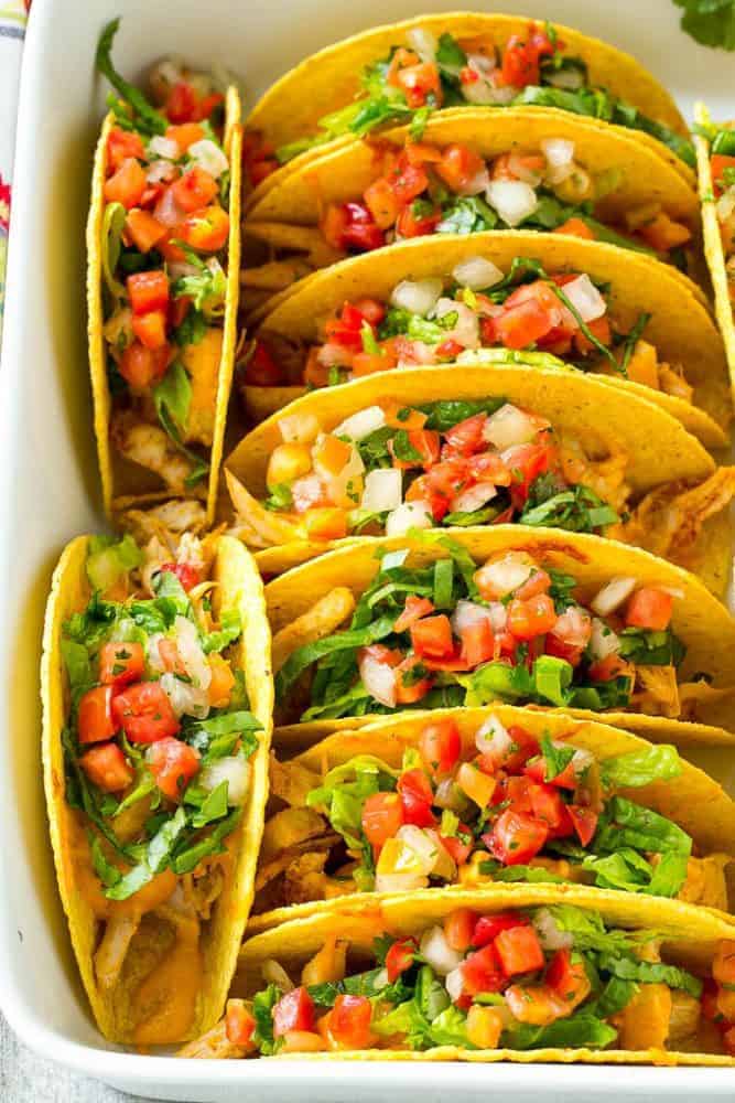 Baked Chicken Tacos stacked in rows in a baking dish.