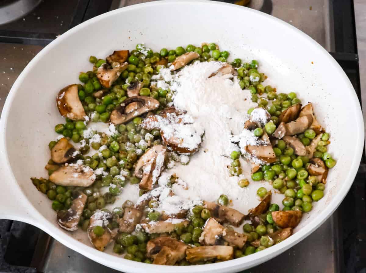 Overhead shot of sautéed mushrooms and peas with flour on top. 