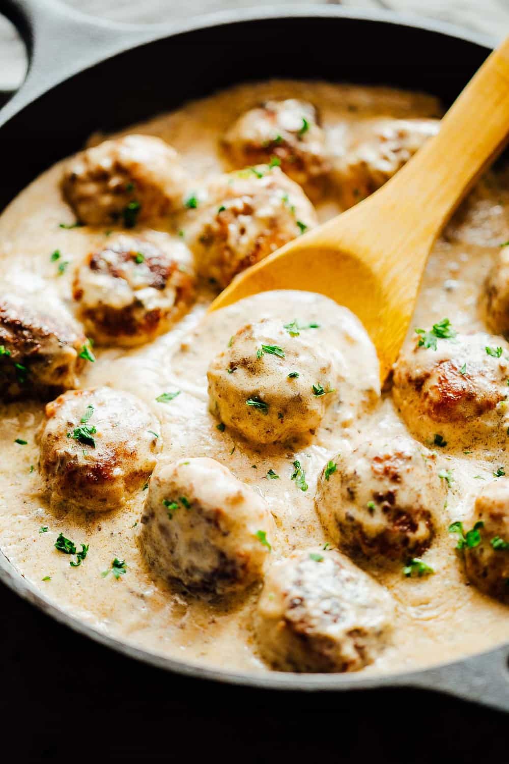 Meatballs in sauce being stirred with a wooden spoon.