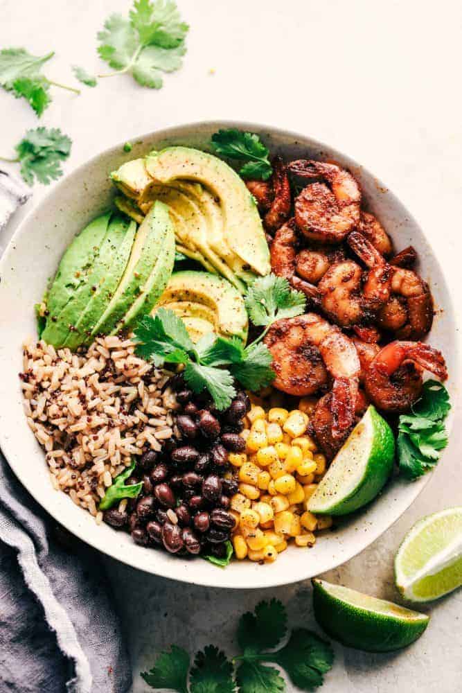 Blackened Shrimp Avocado Burrito Bowl in a white bowl with limes and cilantro on the side. 