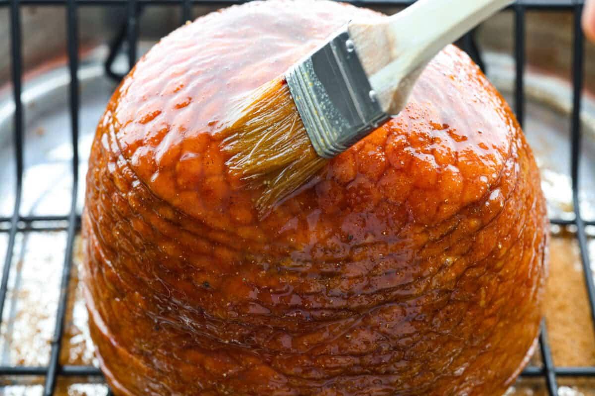 Angle shot of someone basting the pineapple glaze onto the ham. 