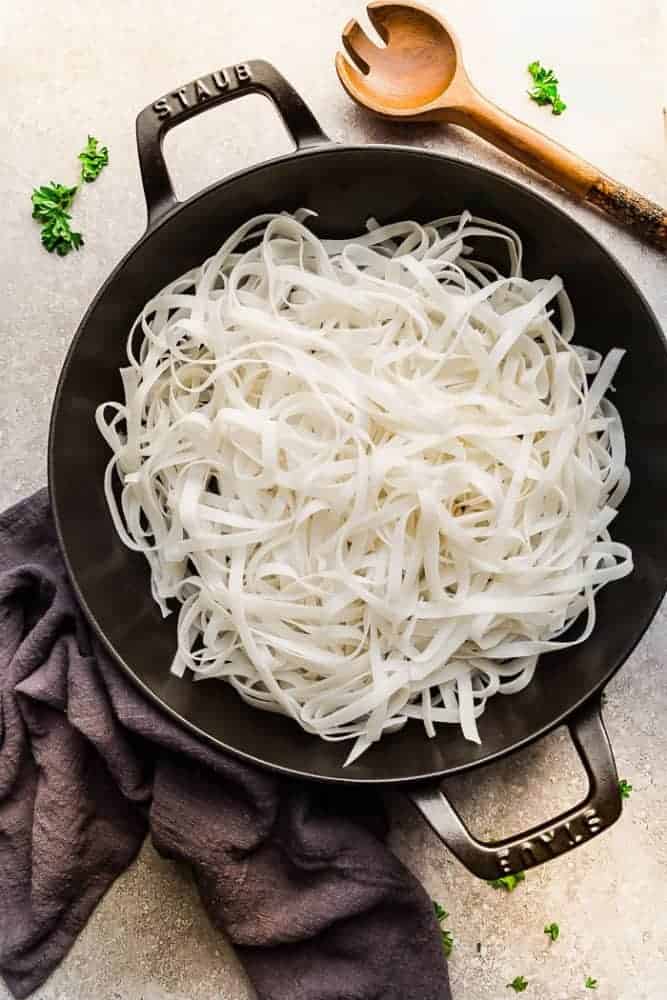 Uncooked noodles in an iron skillet and a wooden spoon next to it. 