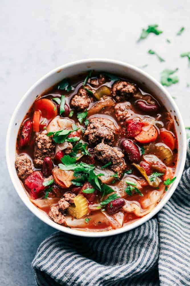 Beef and cabbage soup in a white bowl with a grey and white cloth. 