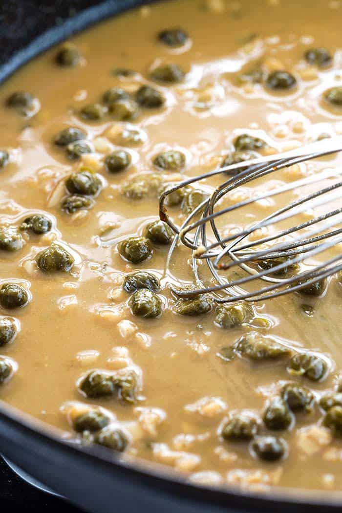 Whisk mixing a lemon caper sauce in a cast iron pan