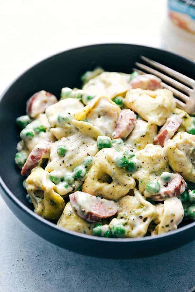 Close up of Alfredo Pesto Tortellini with Sausage in a black bowl. 