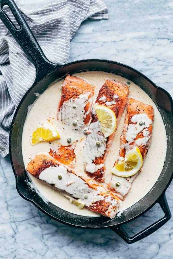 Lemon Salmon Piccata served in a cast iron pan with creamy sauce and lemon slices drizzled all over it