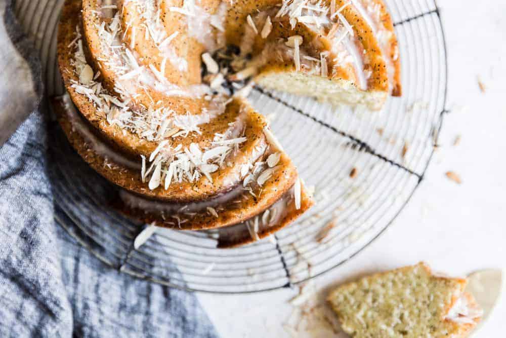 Almond poppyseed bundt cake with a slice removed. The cake is placed on a cooling rack. 