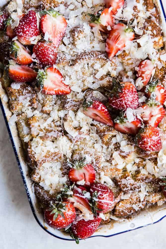 Coconut Bread Pudding in a white pan with fresh cut strawberries on top. 