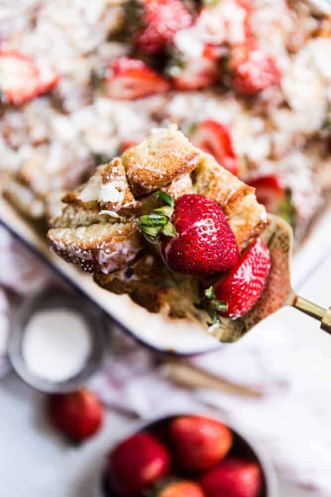 A spoon full of coconut bread pudding with a fresh strawberry on top. 