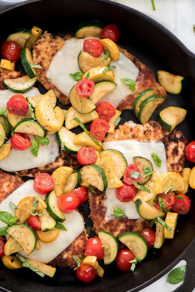 Chicken parmesan with mixed fresh cut vegetables on top in a skillet.