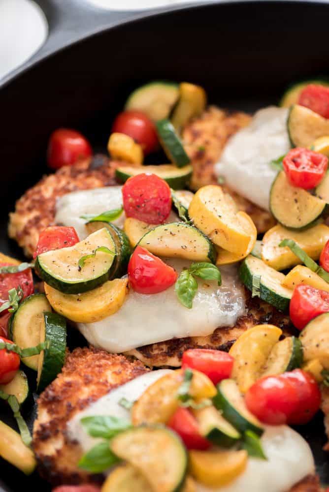 Close up of chicken parmesan with fresh cut vegetables in a skillet. 