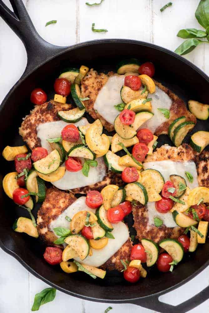 Chicken parmesan with fresh cut vegetables in a skillet. 