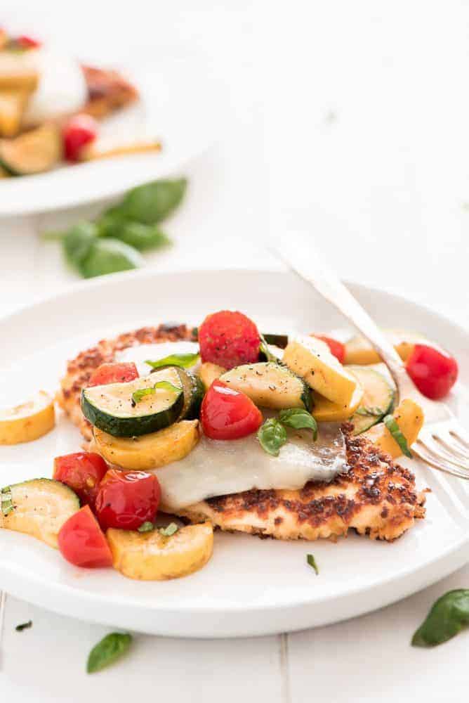 Chicken parmesan on a white plate with mixed fresh vegetables on top. 