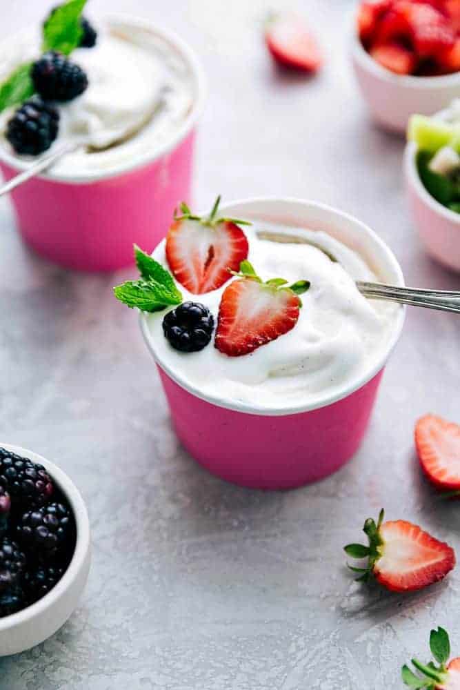 Two pink paper cups of vanilla soft serve frozen yogurt. One of them has fresh strawberries on top and the other has blackberries on top. 