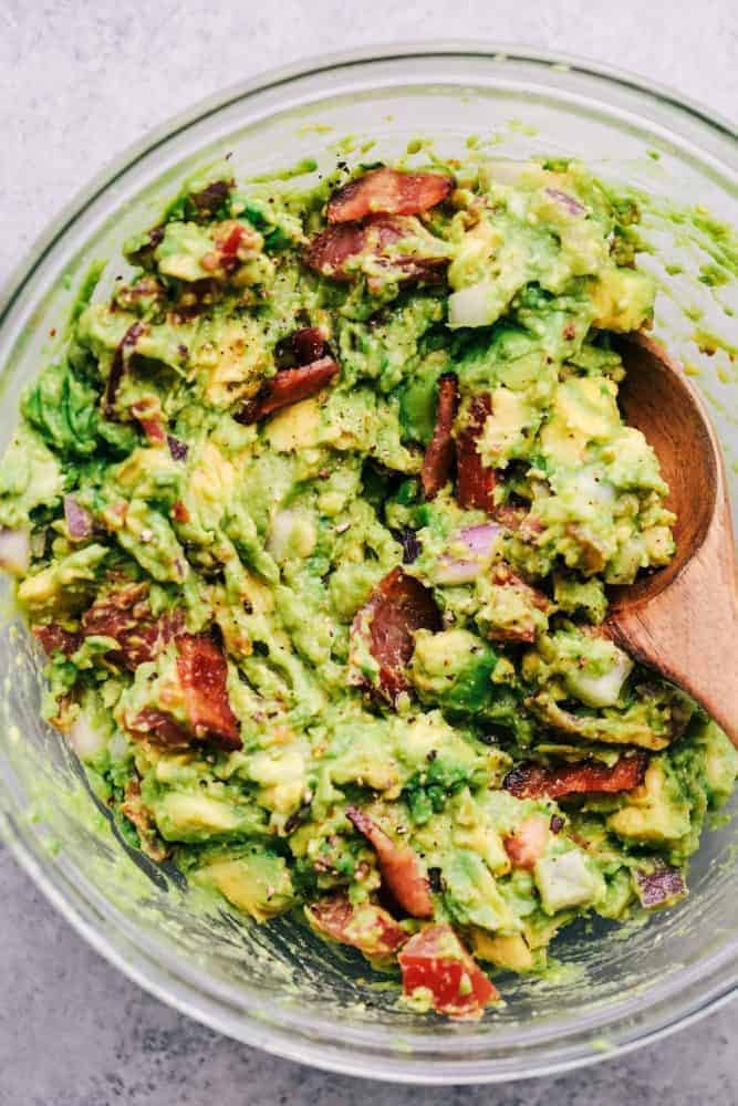 Bacon Guacamole in a white bowl with a wooden spoon. 