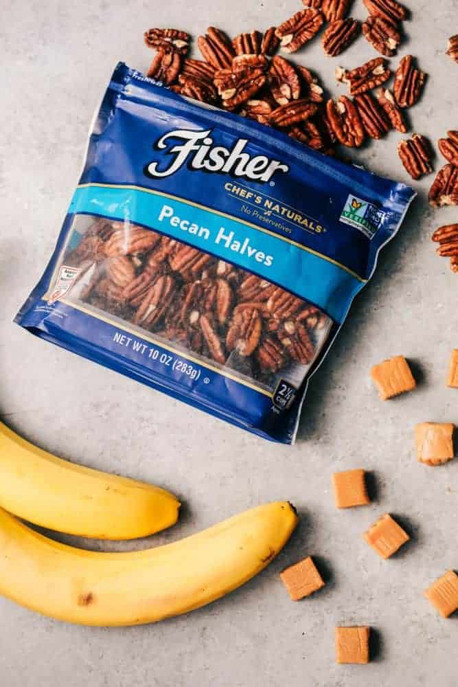 An open bag of pecan halves with two whole bananas and caramels. 