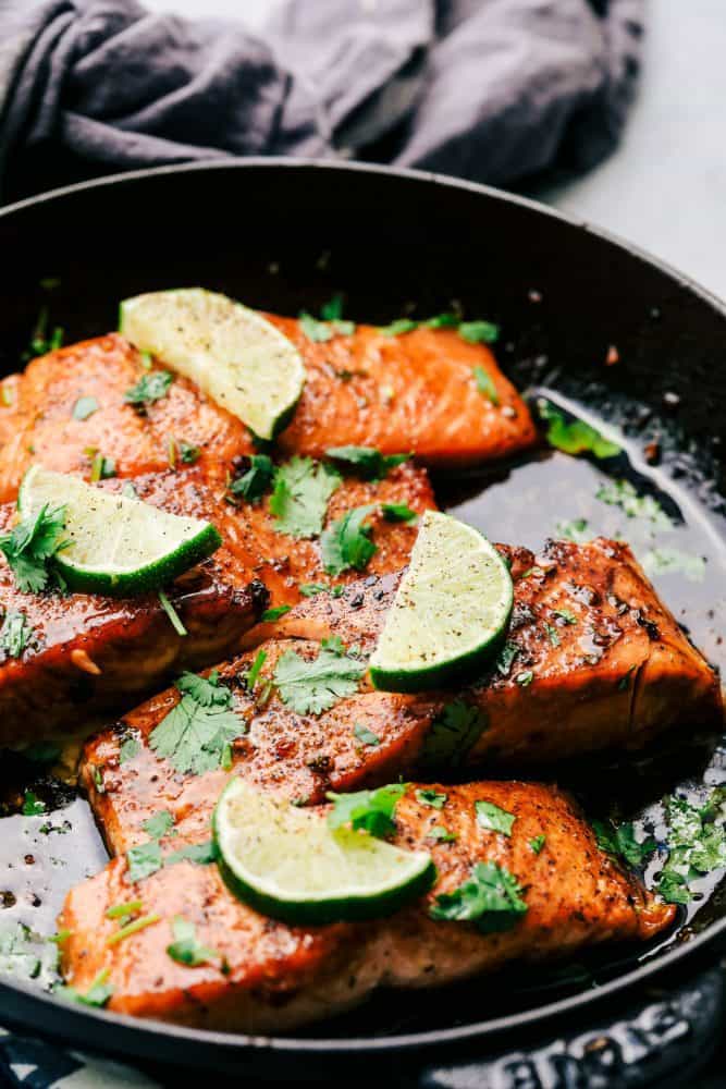 Cilantro Lime Butter Salmon in a skillet with sliced limes on top of the salmon. 