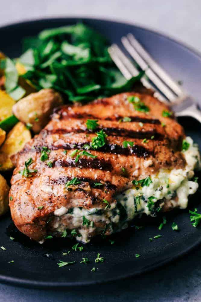 Grilled Spinach and Herb Stuffed Pork Chops on a black plate with a metal fork. 