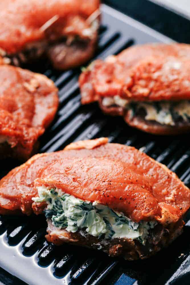 Uncooked herb stuffed pork chops on a grill pan.